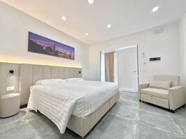 Una habitación de hotel moderna con una cama grande, una silla, una mesita de noche y un cuadro de un paisaje urbano en la pared.