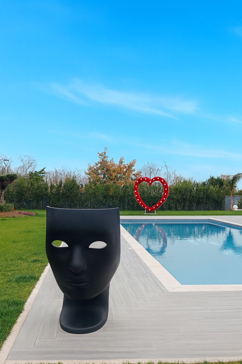A modern outdoor pool area with a large black sculpture in the foreground and a heart-shaped decoration in the background.