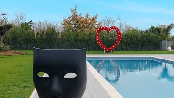 A modern outdoor pool area with a large black sculpture in the foreground and a heart-shaped decoration in the background.