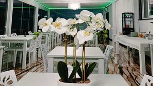 A modern dining area with white tables and chairs, a central orchid plant, and a chandelier. - Hotel Ohana (Rome)
