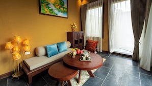 A living room with a sofa, a round coffee table, a floor lamp, a painting, and a window with curtains. - Cometa Villas Ninh Bình (Gia Phong)