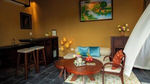 A cozy bar area with stools, a sofa, and a dining table with a vase of flowers. - Cometa Villas Ninh Bình (Gia Phong)