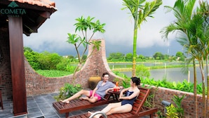 A couple relaxing on wooden loungers by a poolside, with a brick structure and lush greenery in the background. - Cometa Villas Ninh Bình (Gia Phong)