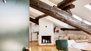 Una habitación tipo ático con vigas de madera a la vista, chimenea, mesa de comedor y una silla verde.