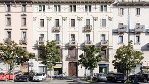 Una hilera de edificios de varios pisos con balcones, coches aparcados y árboles.