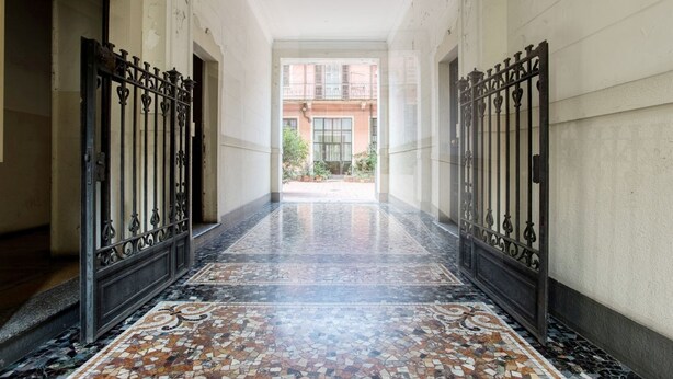 Un pasillo con piso de baldosas que conduce a un edificio con balcón.