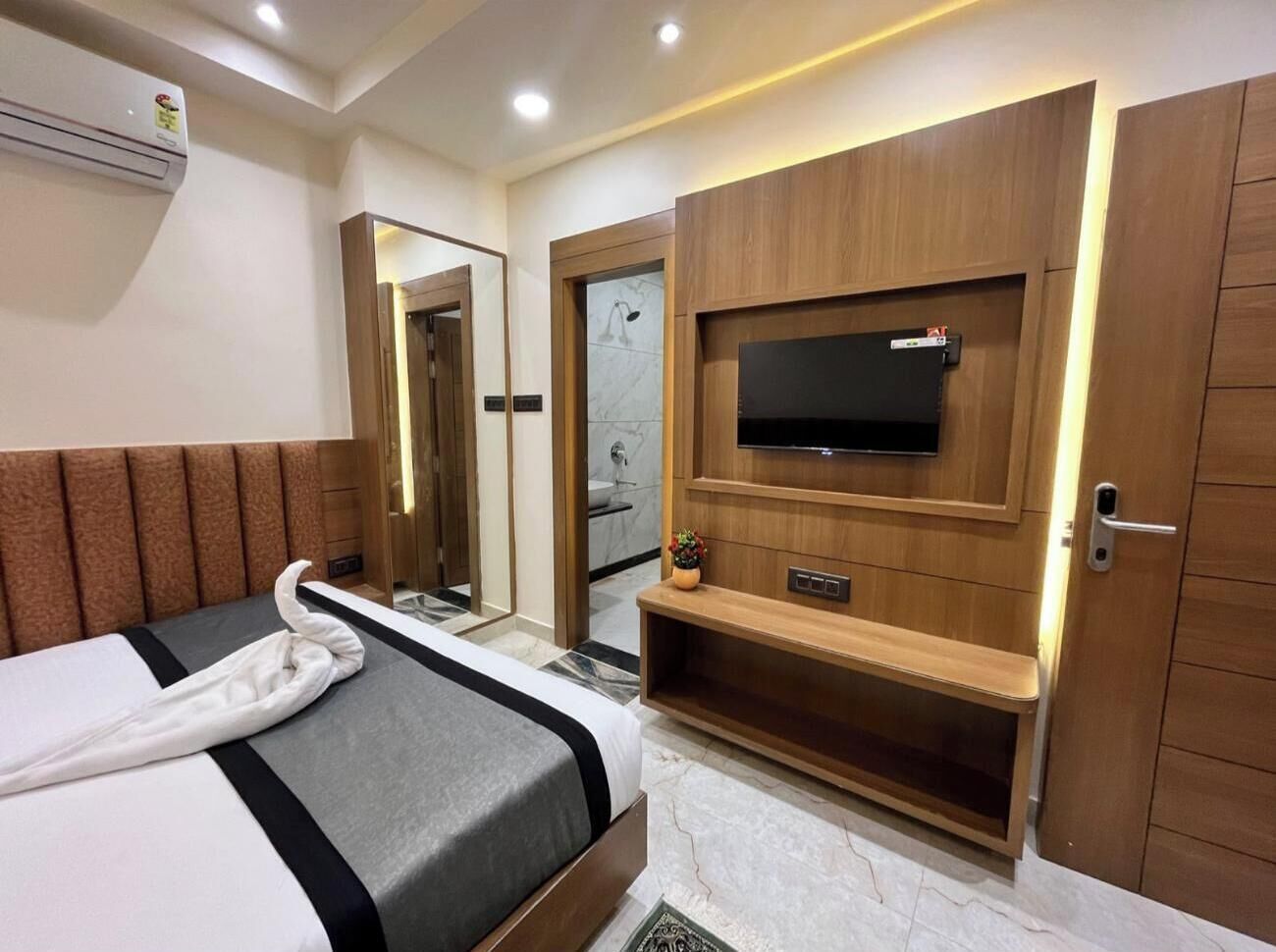 A hotel room with a bed, a TV mounted on a wooden panel, a shower area, and a door with a handle.