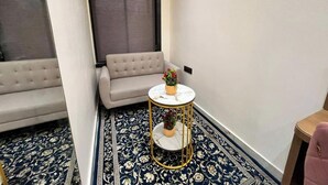 A small, elegantly furnished room with a sofa, a round table with a vase of flowers, and patterned carpet. - Hotel prime bliss (Kanpur)