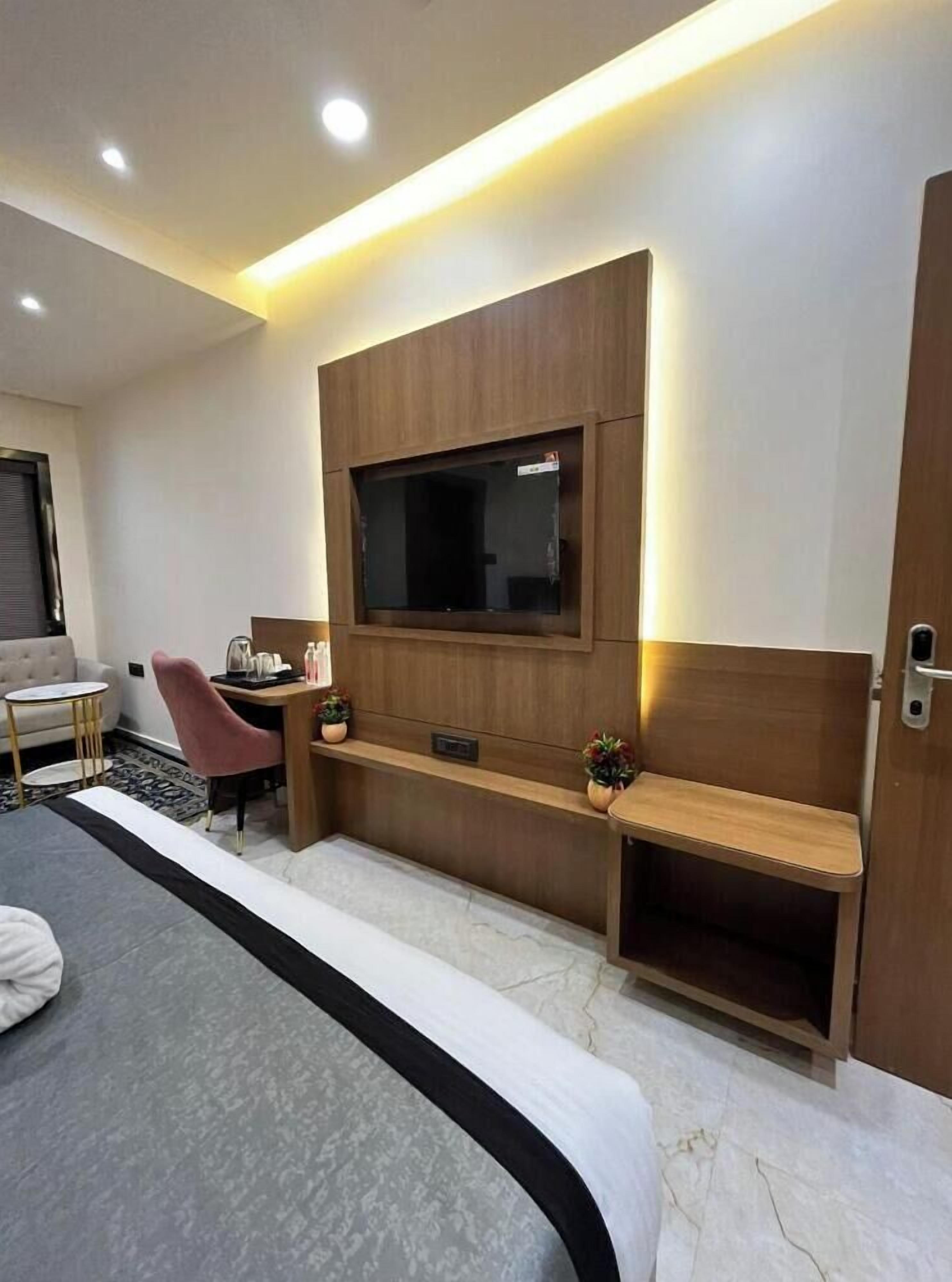 Une chambre d’hôtel moderne dotée d’un grand lit, d’un bureau avec une chaise, d’un téléviseur fixé au mur et d’un petit coin salon avec un banc.
