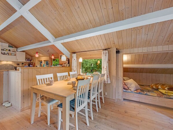 A cozy wooden cabin interior with a dining area, kitchen, and a sleeping loft.