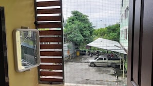 A view through a window with a metal grid, a wooden slat door, and a metal window frame. - Natcha Place Klongluang 35 (Khlong Luang)
