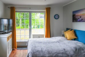 Ett sovrum med en säng, en tv och utsikt över naturen genom en glasdörr.