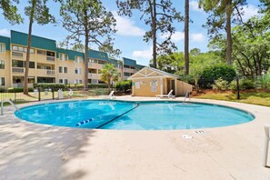 A swimming pool with a lifeguard station, lounge chairs, and a building with balconies in the background. - Beach Bliss Villa with Scenic Ocean Views (Hilton Head Island)