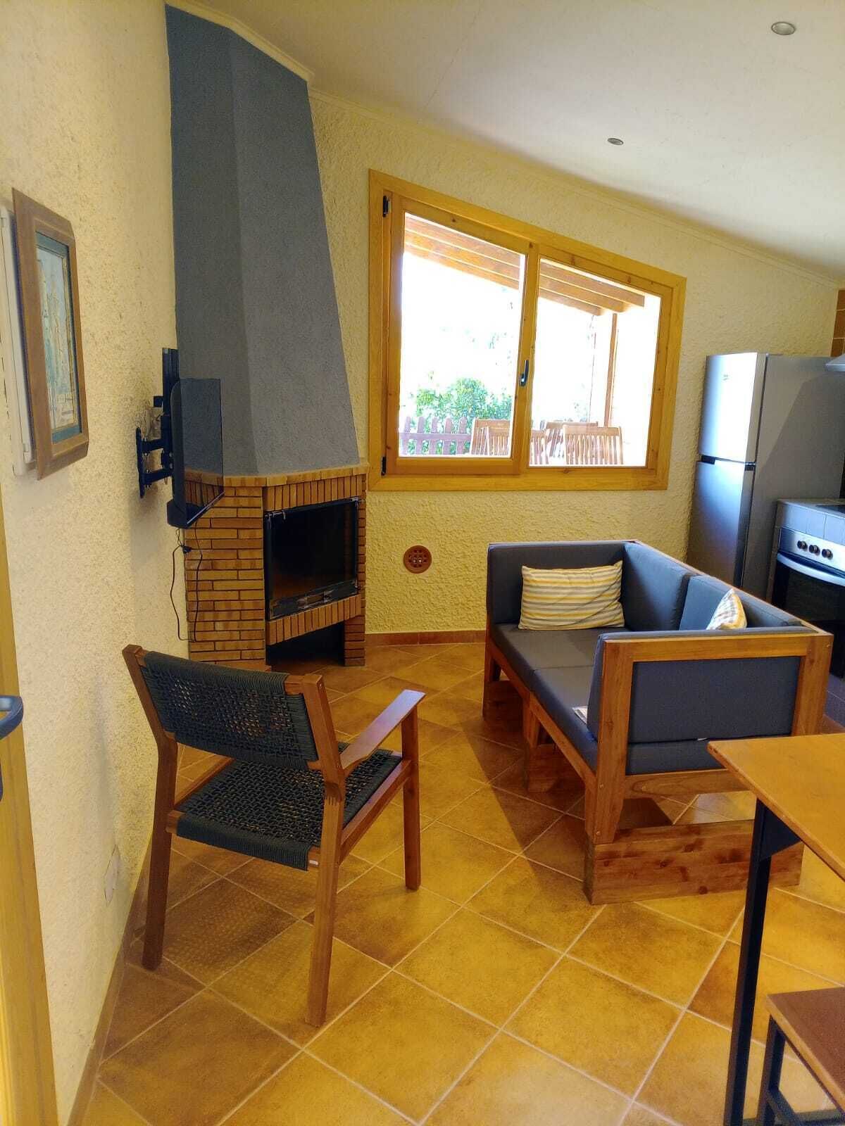 Uma sala de estar com lareira, sofá, poltrona, mesa e geladeira.