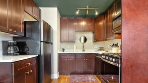 Une cuisine avec des meubles de rangement en bois foncé, un réfrigérateur en acier inoxydable, une cuisinière et une machine à café.