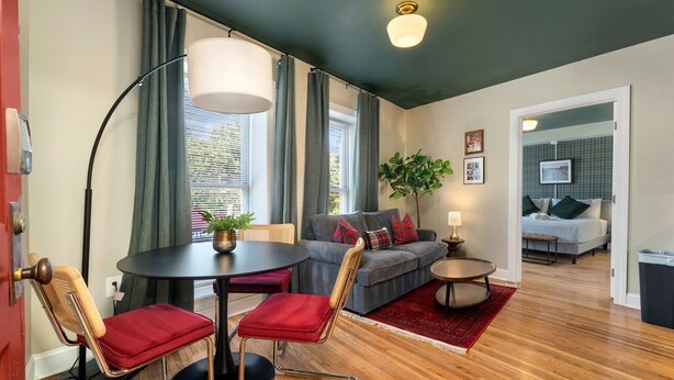 Un salon moderne avec une table de salle à manger ronde, deux chaises, un canapé, une petite table d’appoint et une plante en pot.