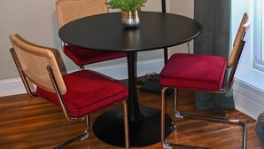 Une pièce avec une table ronde, deux chaises rouges à coussins, un lampadaire et une plante en pot.