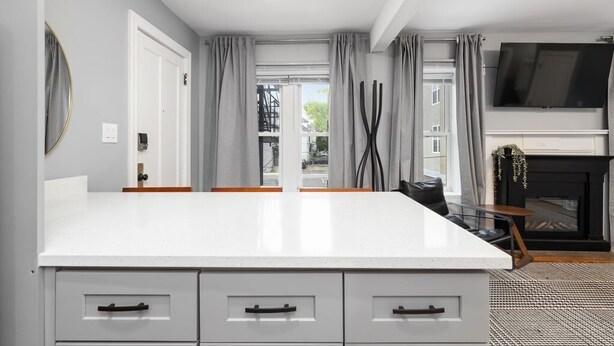 Une cuisine moderne avec un plan de travail blanc, des meubles gris et une cheminée.