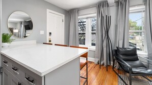 Une cuisine moderne avec un plan de travail blanc, des chaises en bois et un fauteuil en cuir noir.