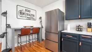 A modern kitchen with a stainless steel refrigerator, dark cabinets, and a bar stool area.