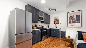 A modern kitchen with dark cabinets, stainless steel appliances, and a wooden floor.