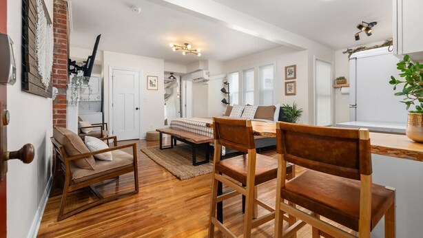 A spacious living area with a wooden floor, a dining table, and two wooden chairs. There is a bench and a sofa in the background. - Modern Loft In the Heart of OSU Campus (Columbus)