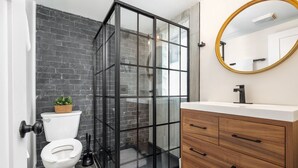 A bathroom with a glass shower enclosure, a white toilet, a wooden vanity with drawers, and a round mirror. - Modern Loft In the Heart of OSU Campus (Columbus)