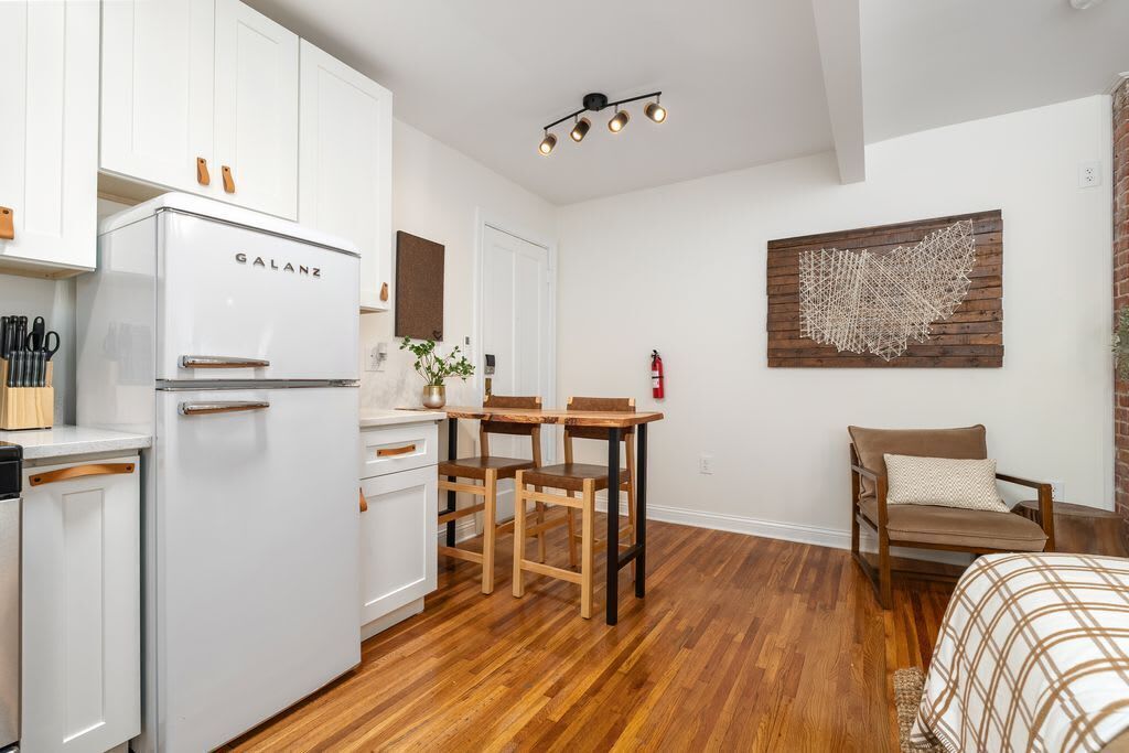 A compact kitchen with a white refrigerator, wooden dining table, and chairs.