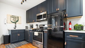 Une cuisine moderne avec des meubles de couleur sombre, des appareils électroménagers en acier inoxydable et un plancher en bois.