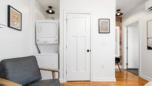 Un couloir avec un canapé gris, une porte blanche et un lave-linge.
