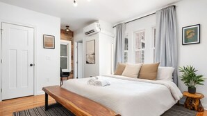 Une chambre avec un grand lit, un banc en bois, une plante en pot et une vue sur un mur de briques et une fenêtre.