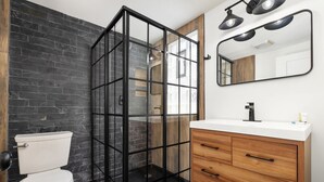 Une salle de bain au design moderne, dotée d’une douche à parois de verre, de toilettes blanches et d’un meuble-lavabo en bois avec un miroir.