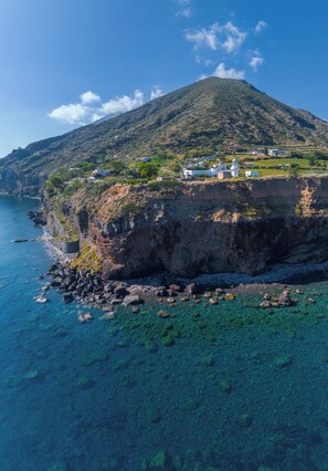 A coastal landscape with a mountain, clear blue sea, and buildings on the cliff.