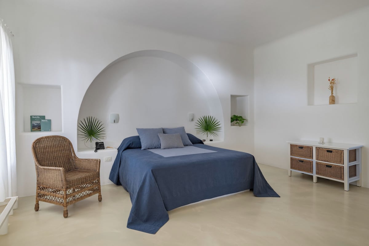 Ein modernes Schlafzimmer mit einem großen Bett, einem Korbsessel, einer weißen Kommode und einer gewölbten Decke.