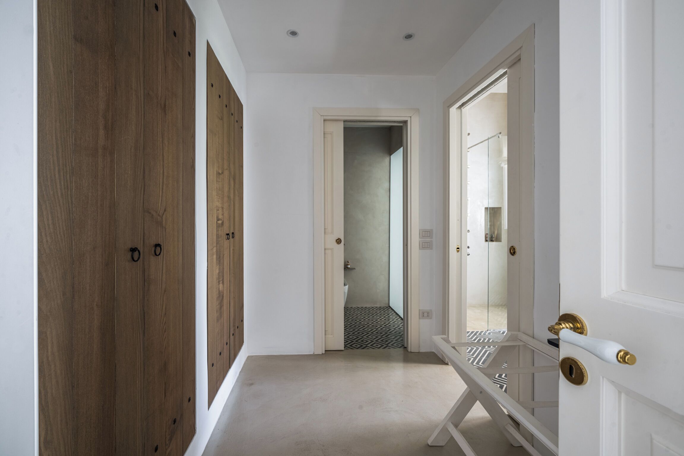 A hallway with wooden doors, a white door leading to a bathroom, and a white door with a brass handle.