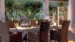 Un restaurant avec des chaises et des tables en osier, des piliers blancs et des plantes en pot.