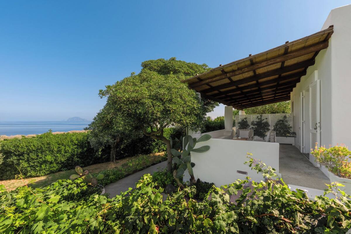 Eine Villa mit weißer Fassade, einer Holzpergola und Meerblick.