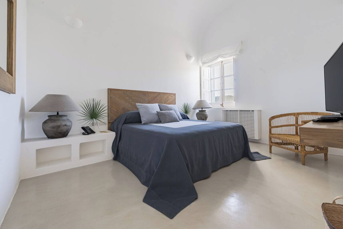 Ein modernes Schlafzimmer mit einem Bett, Nachttischen, einer Lampe, einer Pflanze und einem Korbstuhl.