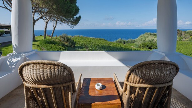 Une terrasse dotée de chaises et d’une table en osier, offrant une vue panoramique sur la mer et la verdure.