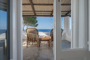 A balcony with wicker chairs and a table, overlooking the sea.