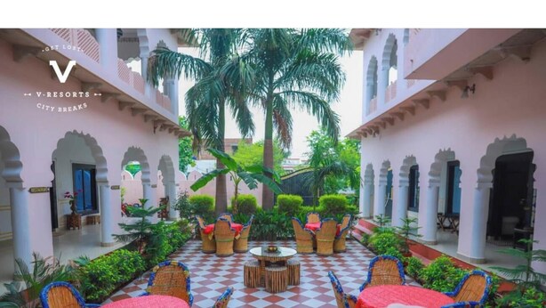 A courtyard with checkered flooring, wicker furniture, and palm trees. - Hotel Kiran Villa Palace (Bharatpur)