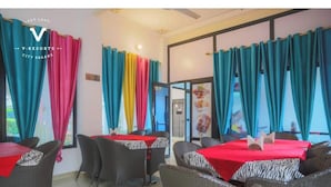 A restaurant with tables covered in red tablecloths, surrounded by wicker chairs. - Hotel Kiran Villa Palace (Bharatpur)