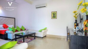 A modern living room with a sofa, a coffee table, and a TV stand with decorative items. - Hotel Kiran Villa Palace (Bharatpur)