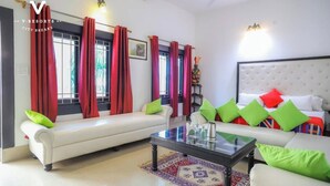 A modern living room with a sofa, a coffee table, and a bed with colorful pillows. - Hotel Kiran Villa Palace (Bharatpur)