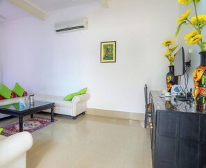 A modern living room with a sofa, a coffee table, and a TV stand with decorative items. - Hotel Kiran Villa Palace (Bharatpur)