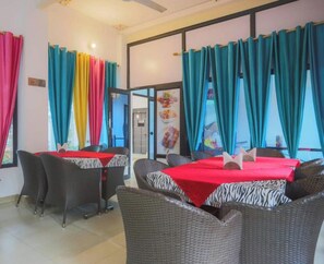 A restaurant with tables covered in red tablecloths, surrounded by wicker chairs. - Hotel Kiran Villa Palace (Bharatpur)