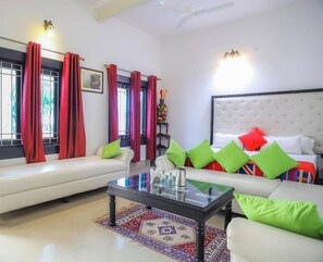 A modern living room with a sofa, a coffee table, and a bed with colorful pillows. - Hotel Kiran Villa Palace (Bharatpur)