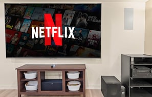 Un televisor de pared mostrando el logotipo de Netflix y un collage de carteles de películas. Abajo, un mueble de madera con cestas de almacenamiento.