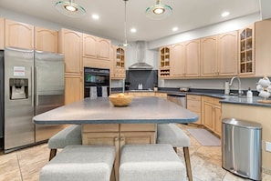 Una cocina moderna con una isla central, electrodomésticos de acero inoxidable, armarios de madera e iluminación colgante.