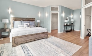 Un dormitorio con una cama de madera, una mesita de noche, un tocador, un espejo y una puerta que da a otra habitación.